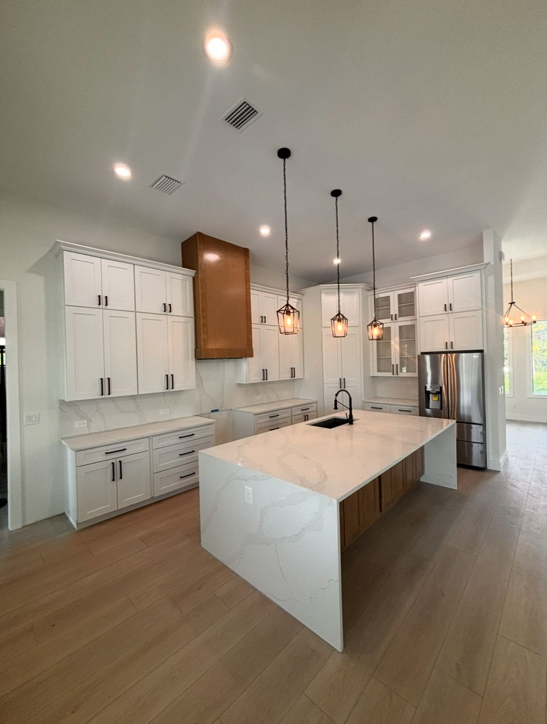 Bright modern kitchen with white cabinets, marble island, pendant lights, and stainless steel fridge