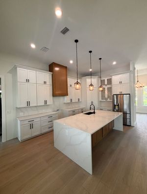 Bright modern kitchen with white cabinets, marble island, pendant lights, and stainless steel fridge