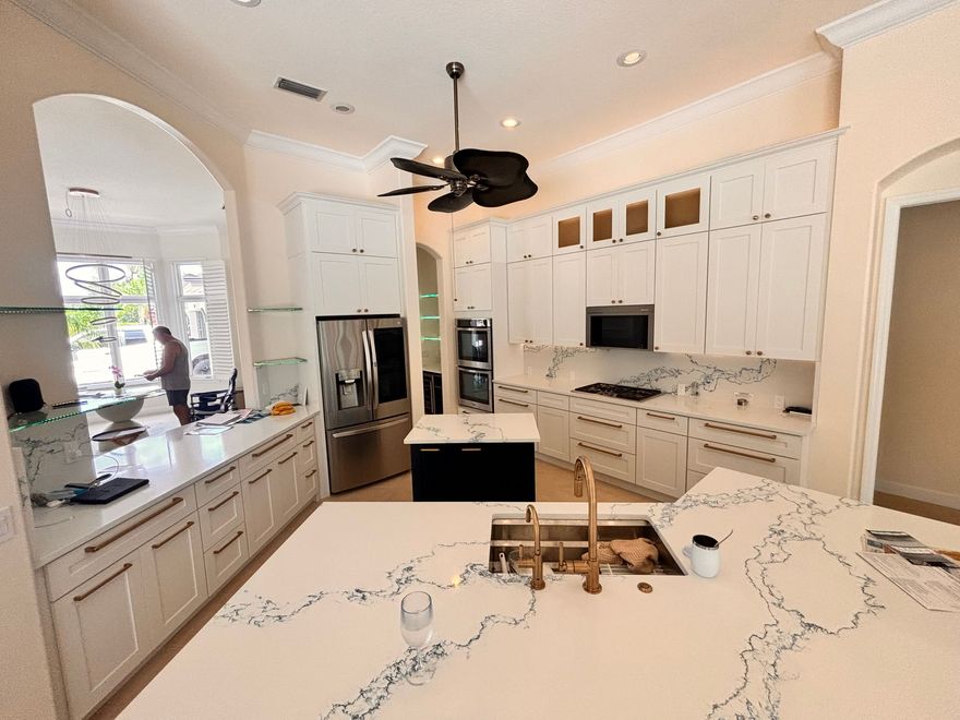 Bright modern kitchen with white cabinets, marble island, and black ceiling fan.