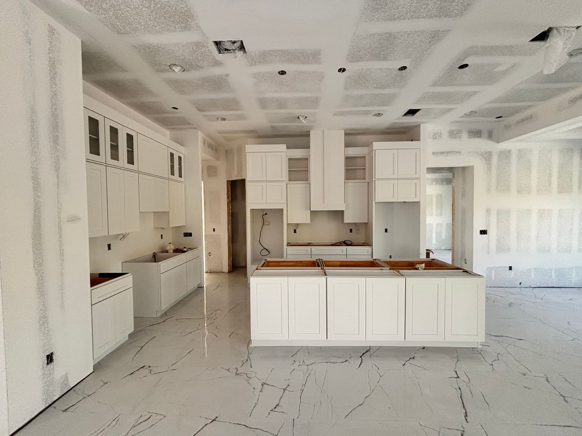 Bright white unfinished kitchen with island, cabinets, and marble-look floor in a spacious room
