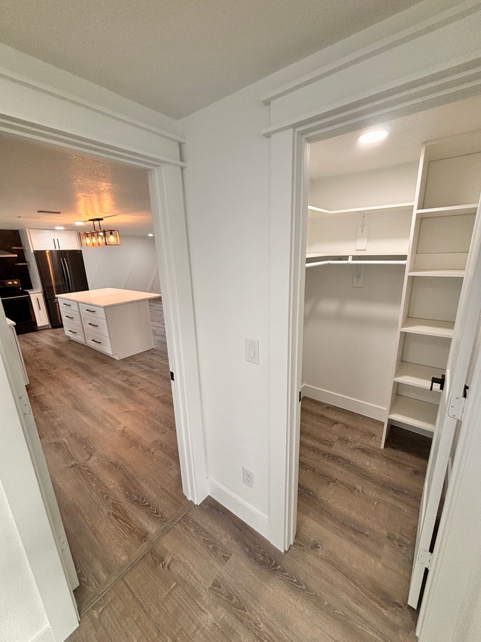 Empty bedroom closet with white shelves and sliding door beside a hallway with wood flooring