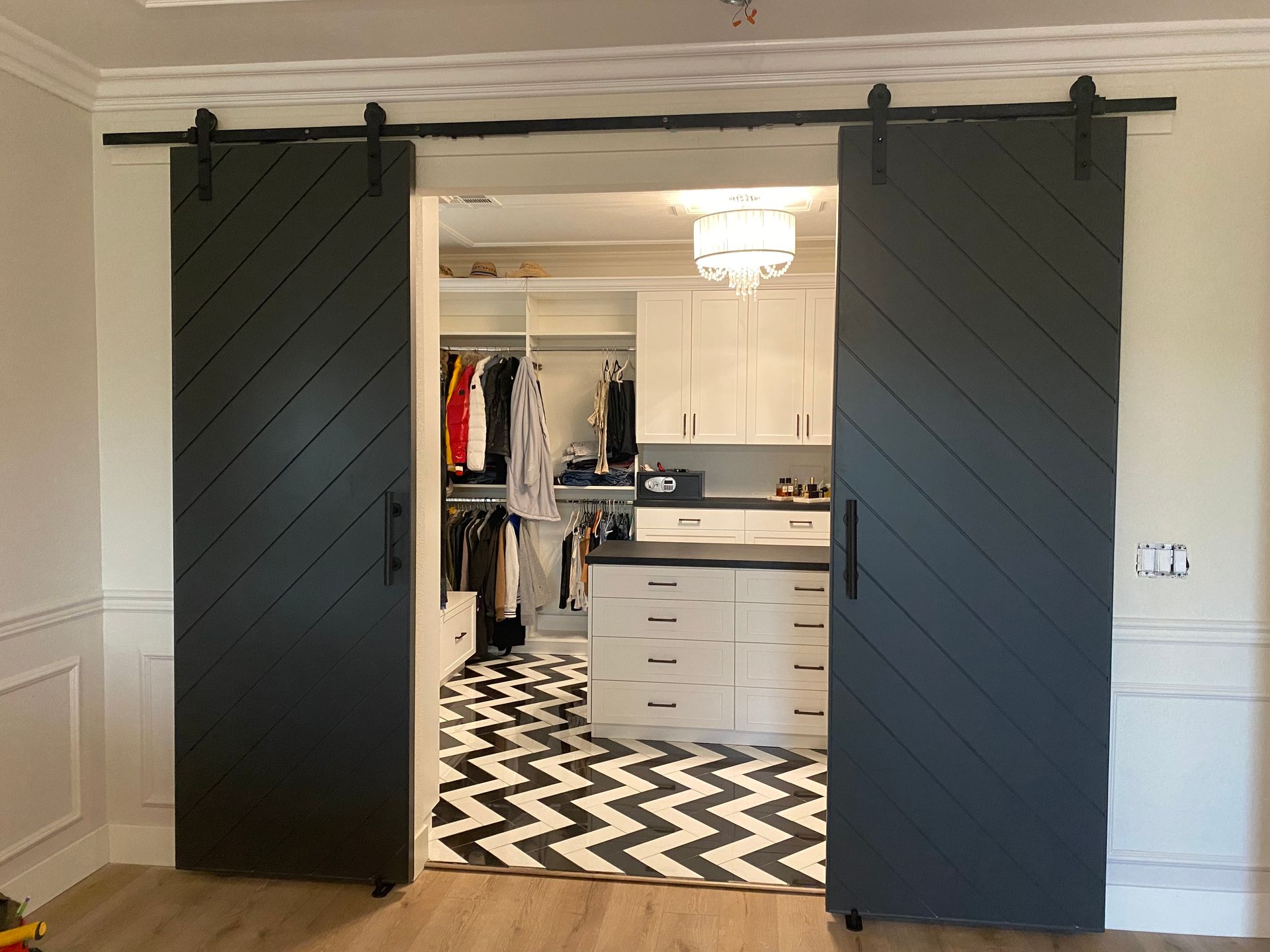 Dark sliding barn doors open to a walk-in closet with white cabinets and black-and-white chevron rug.