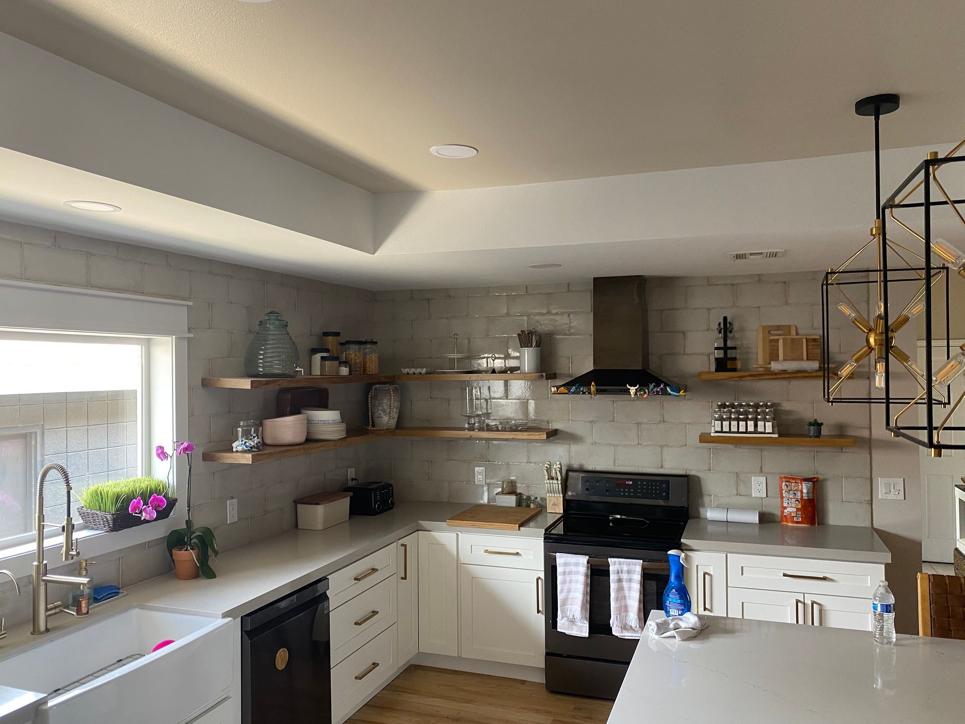 Bright modern kitchen with white cabinets, open shelves, black stove, and hanging pendant lights