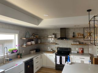 Bright modern kitchen with white cabinets, open shelves, black stove, and hanging pendant lights