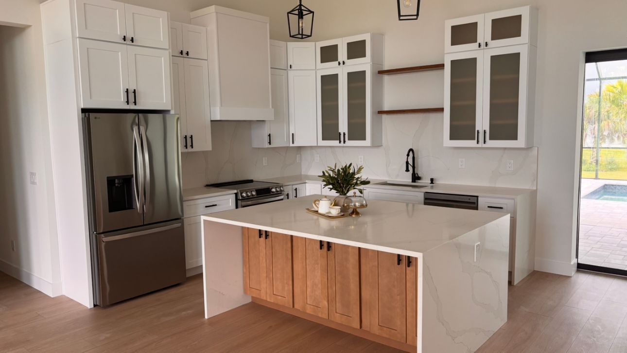 Bright modern kitchen with white cabinets, stainless fridge, marble island, and wood accents.