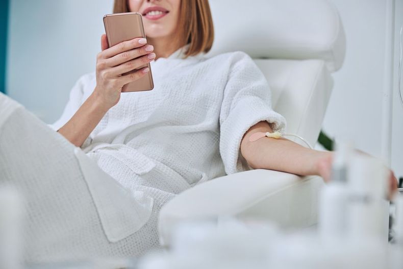 Person lounging on a white chair, looking at a smartphone in a bright room