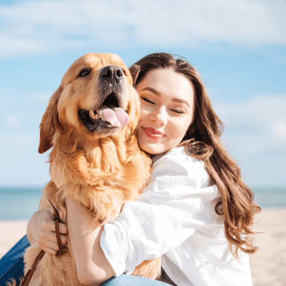 Woman hugging a golden retriever against a bright blue sky, both looking happy