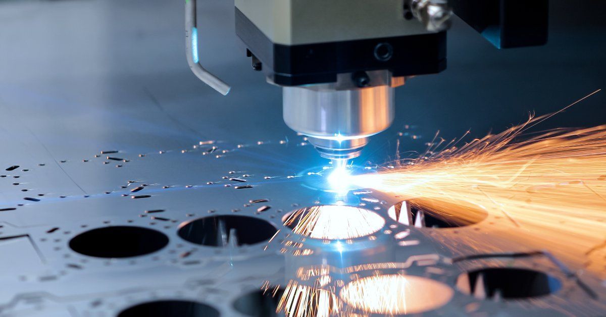 A close-up of a CNC milling machine with a laser in the process of cutting circular pieces out of a sheet of metal.