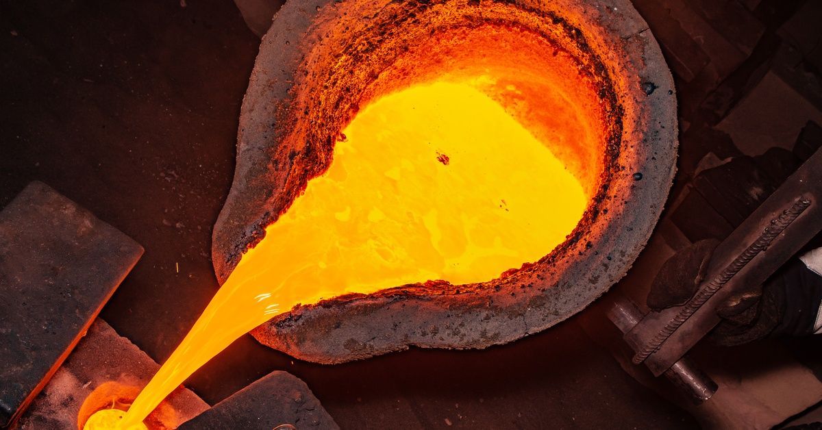 A crucible full of molten metal glowing bright orange, tilting to pour the liquid into a small cast.
