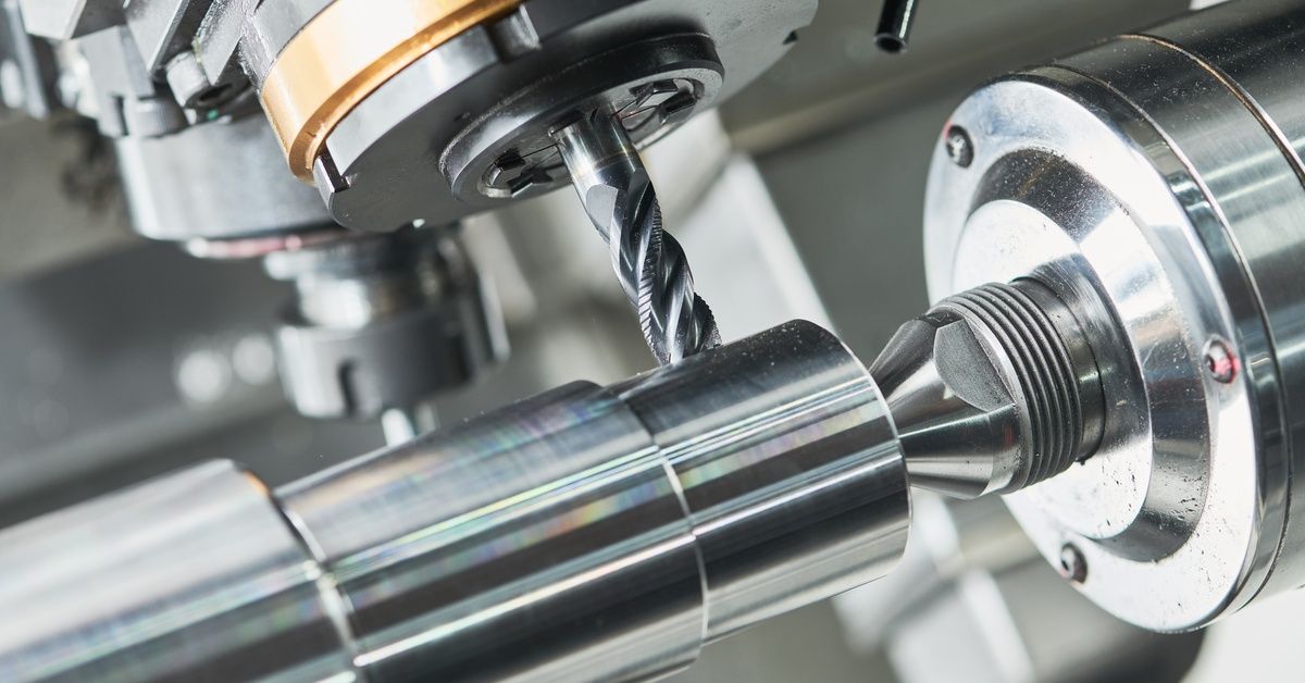 A close-up of a drill cutting tool in a CNC machine removing material from a cylinder of steel.