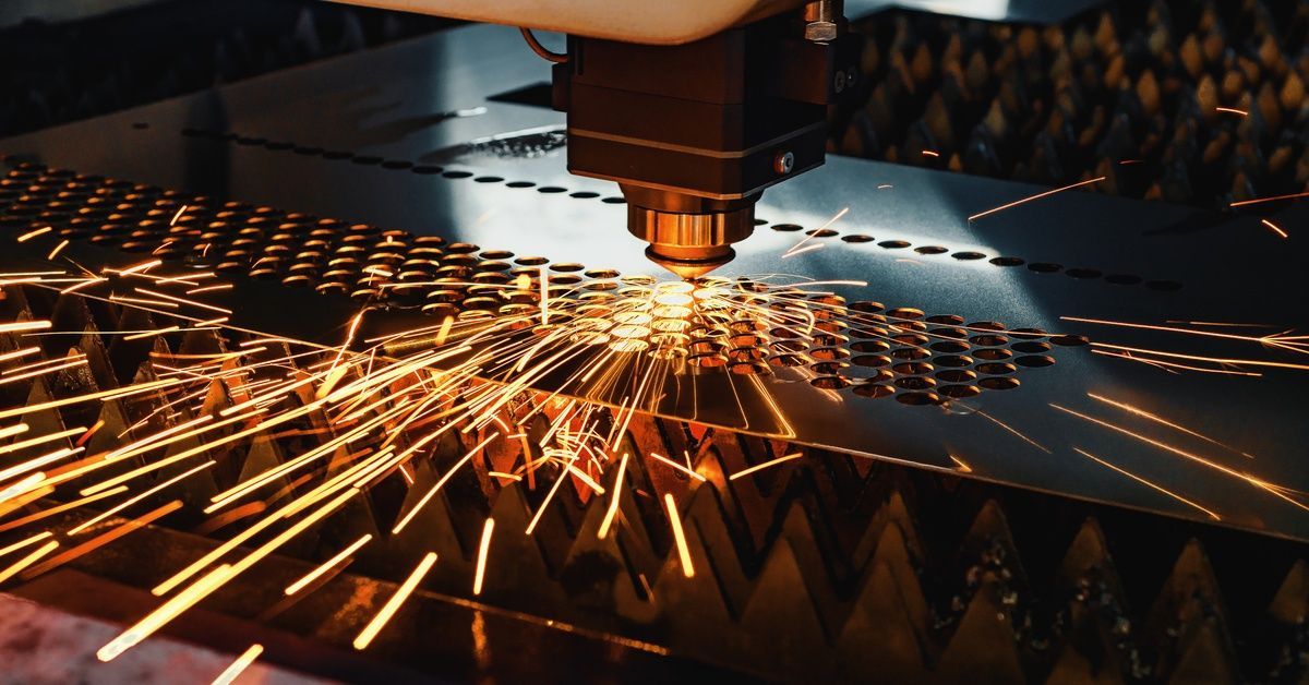 A CNC laser cutting machine creates rows of circular holes on a piece of sheet metal.