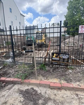 Construction site behind black metal fence with excavator and rubble beside a white building