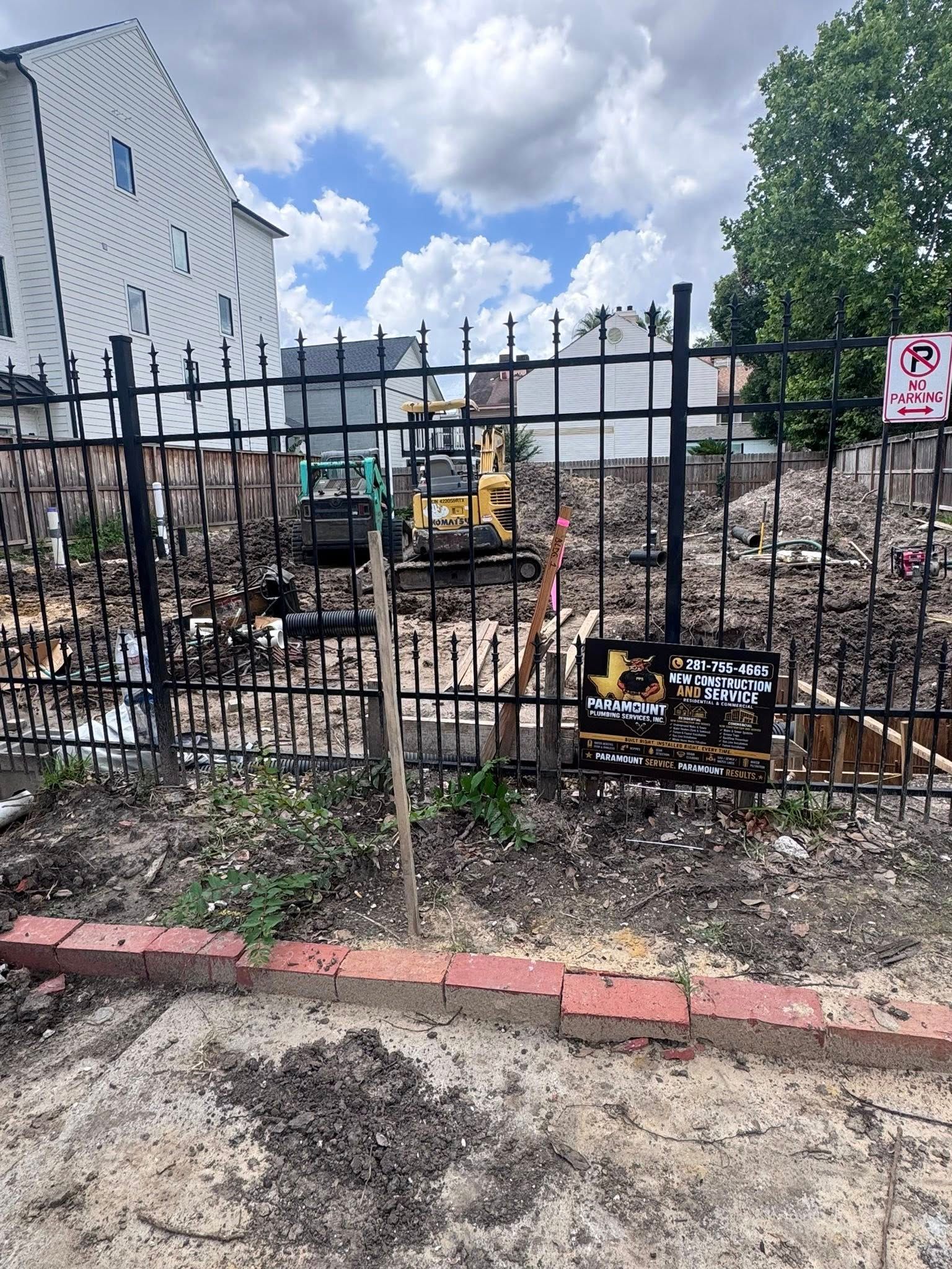 Construction site behind black iron fence beside a white building under a cloudy sky