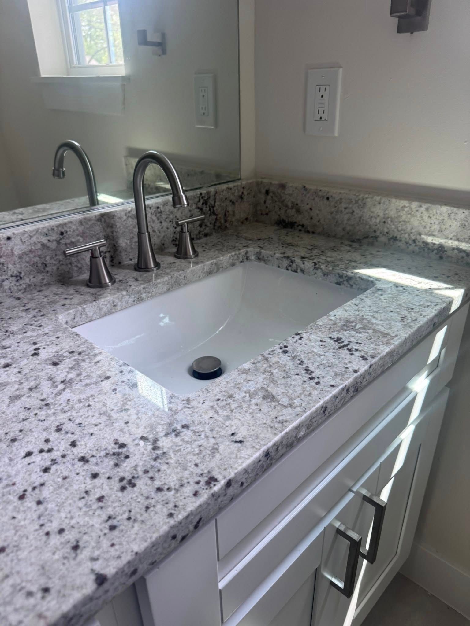 Bathroom vanity with speckled granite countertop, white sink, chrome faucet, and wall mirror.