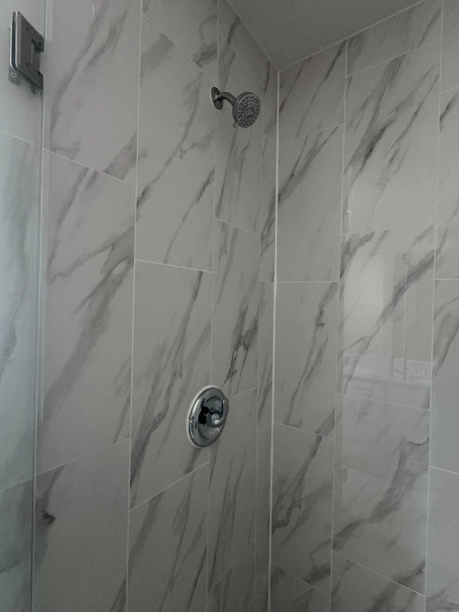Tiled shower corner with chrome showerhead and control knob on marble-pattern walls