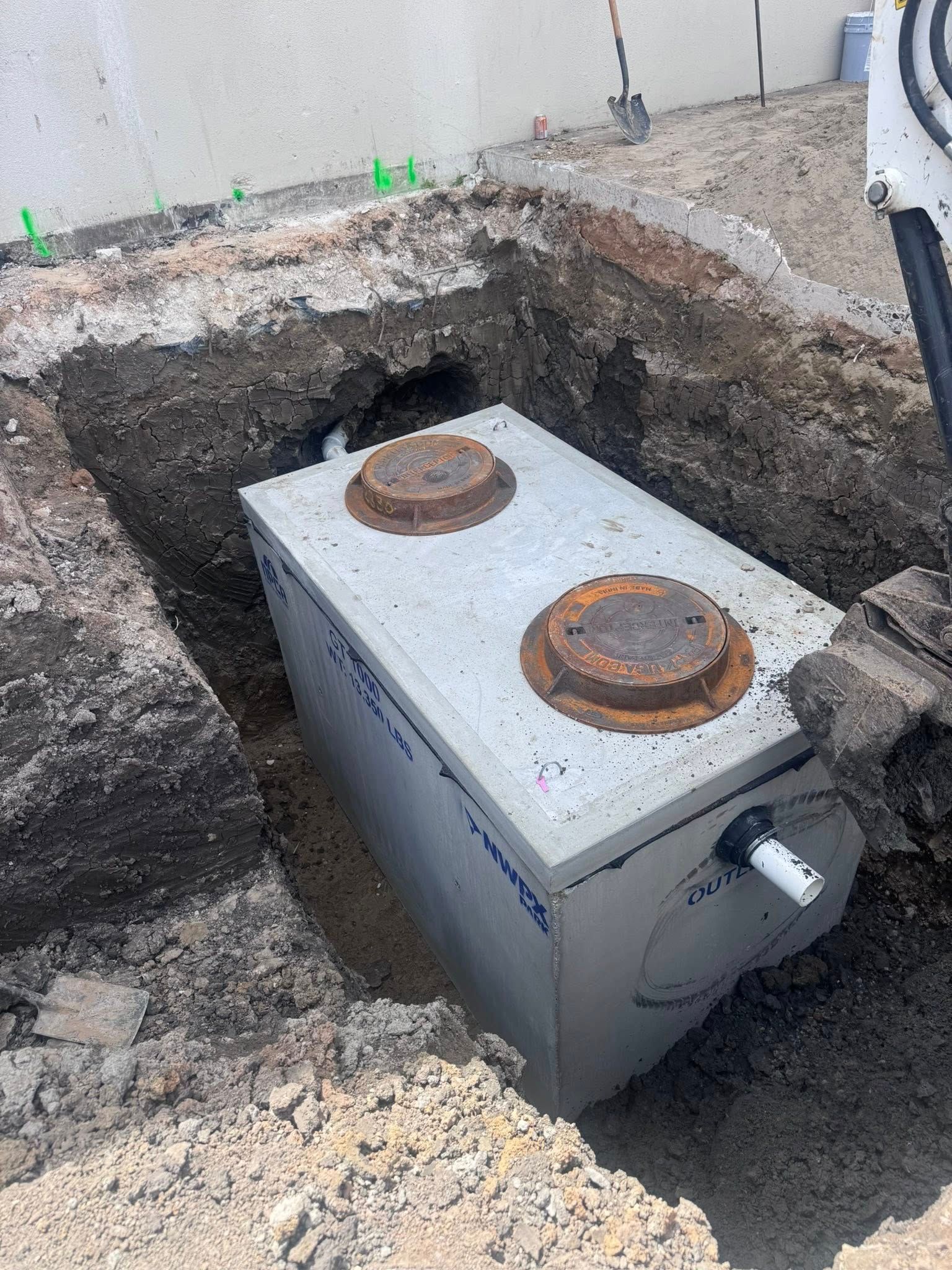 Large metal utility tank in a dirt excavation beside a wall, with two rusted circular caps on top.