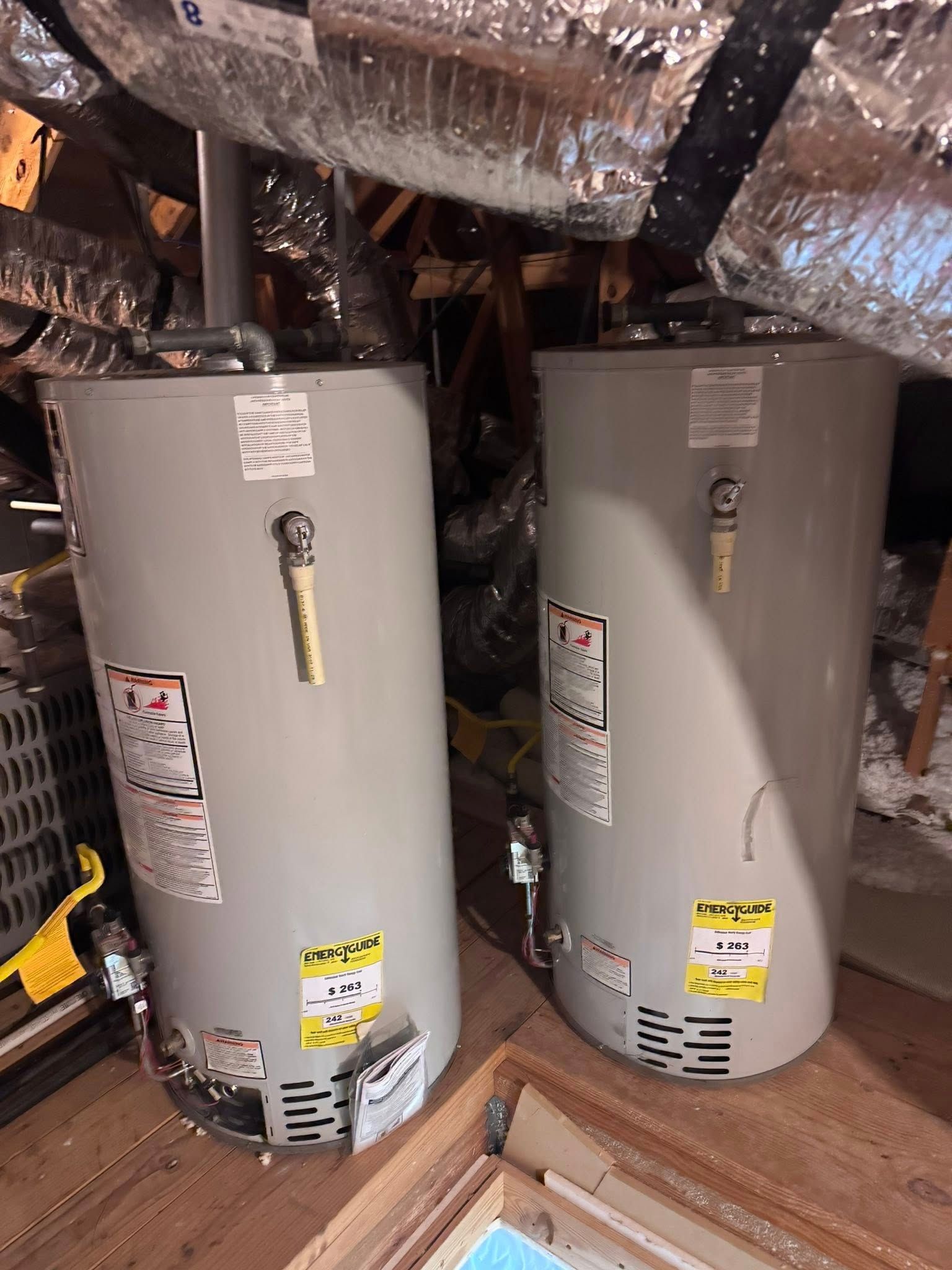 Two gray water heaters in an attic with exposed ductwork and insulation.