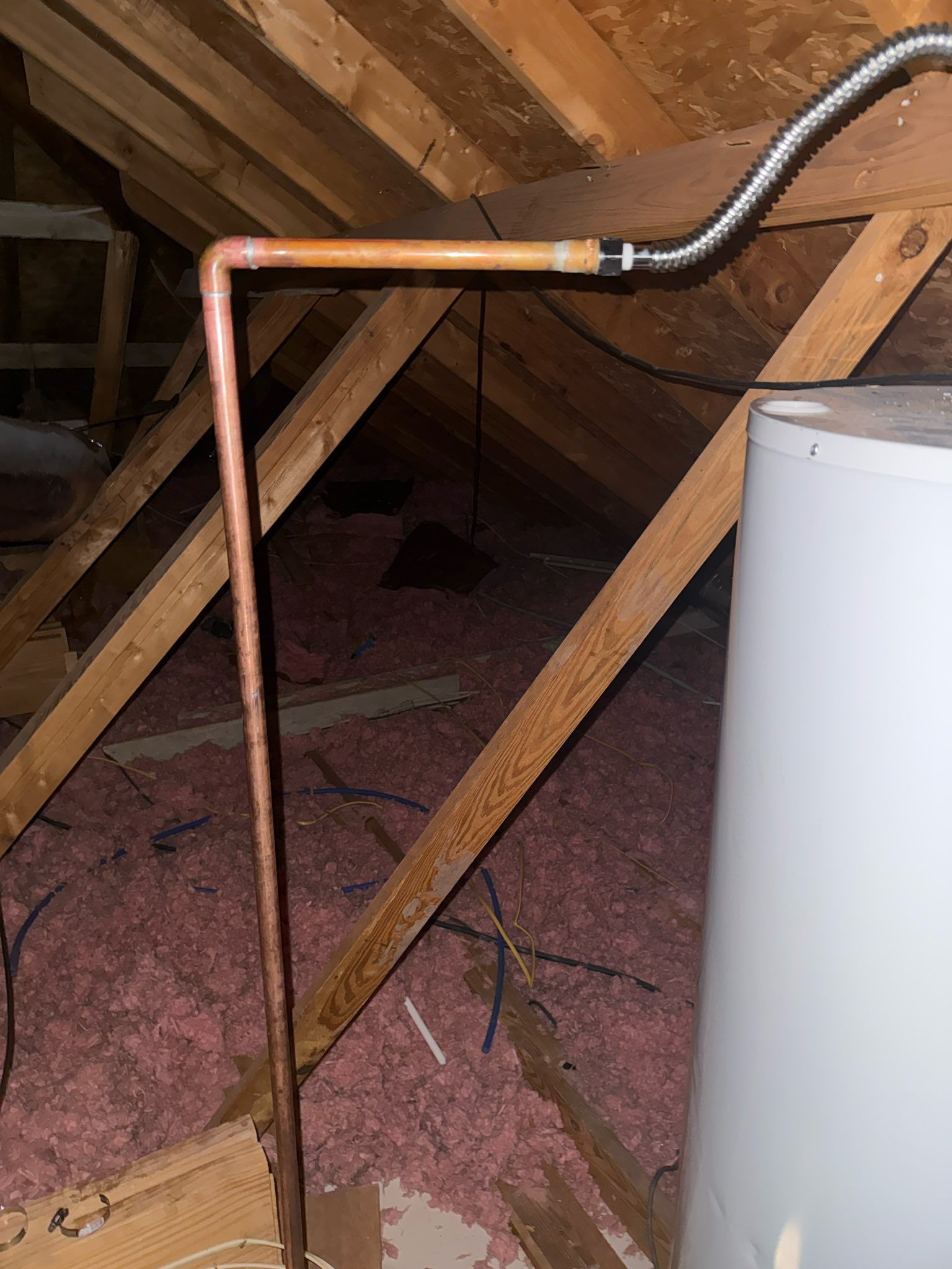 Copper pipe and black hose running through an attic beside a white water heater.