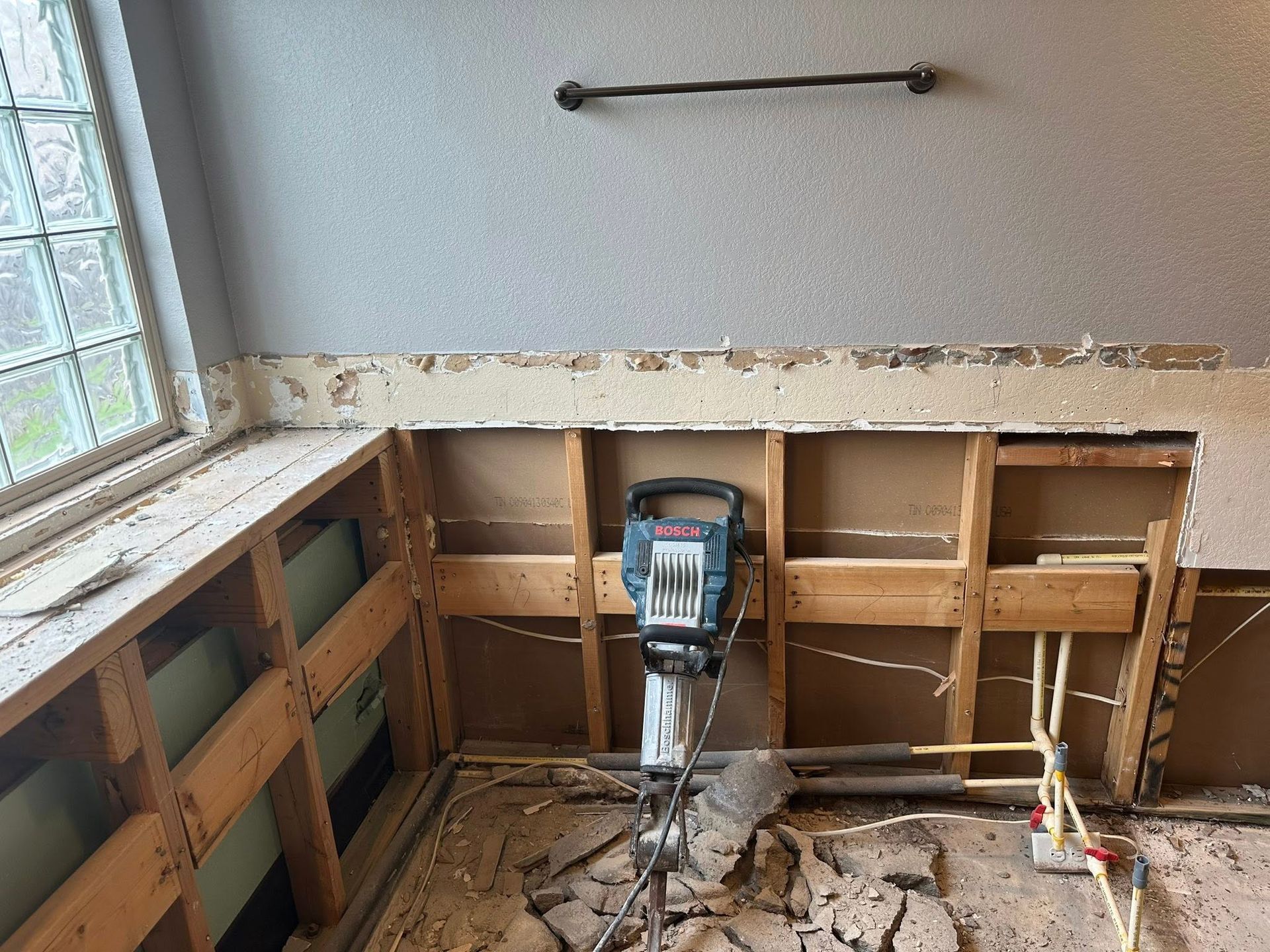 Partially demolished kitchen with exposed framing, sink plumbing, and a power tool on the floor