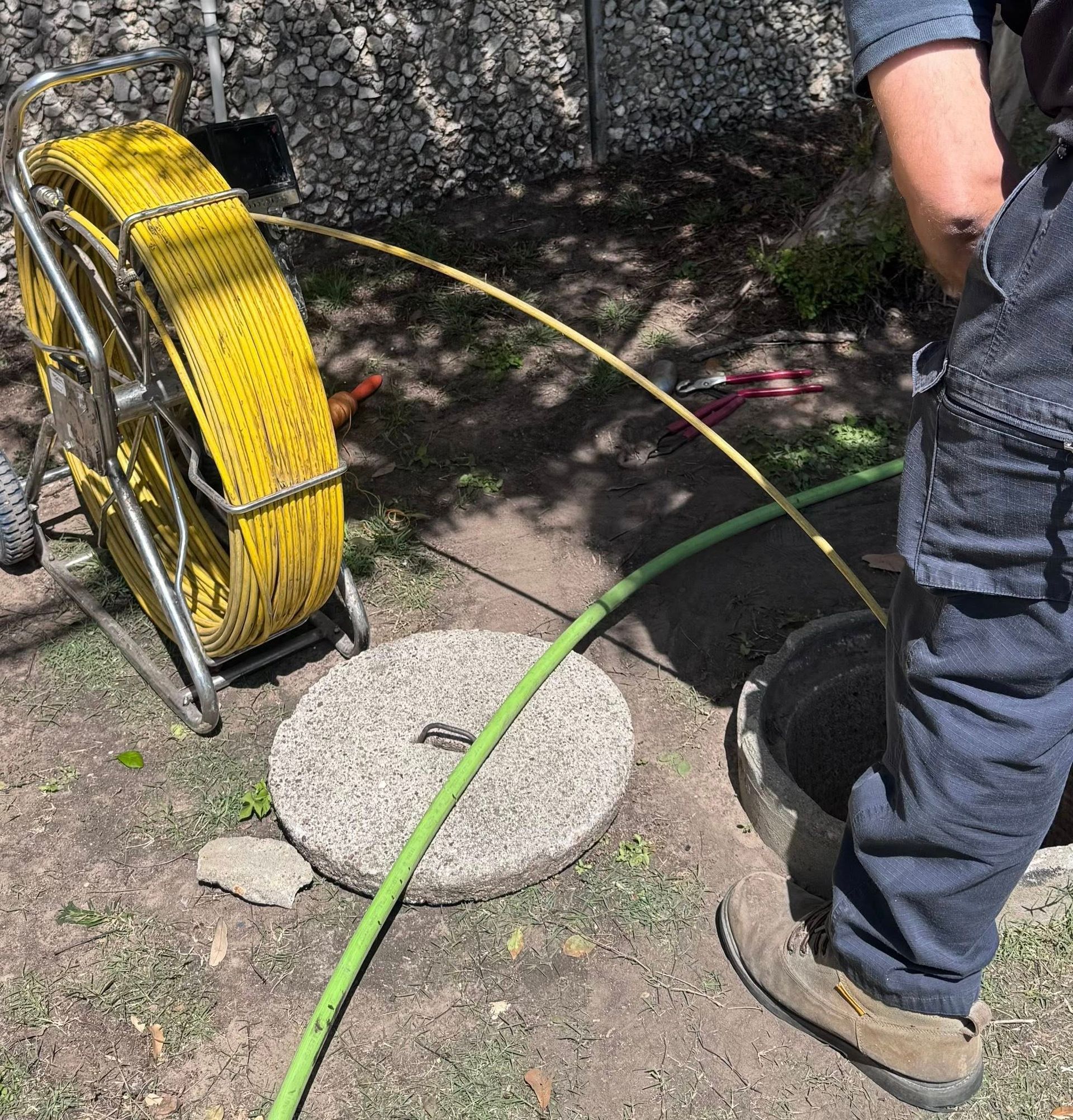 Fiber-optic cable being fed from a yellow reel into an open manhole beside a worker's legs