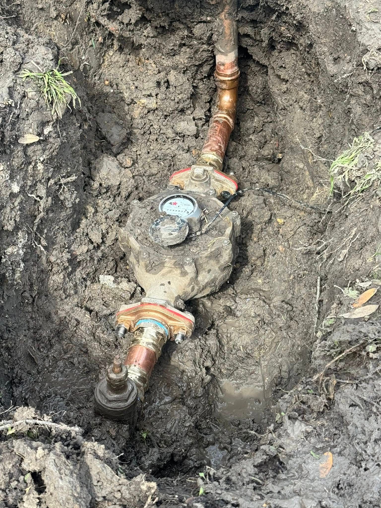 Buried metal pipe joint with rusted fittings and orange rings in muddy ground