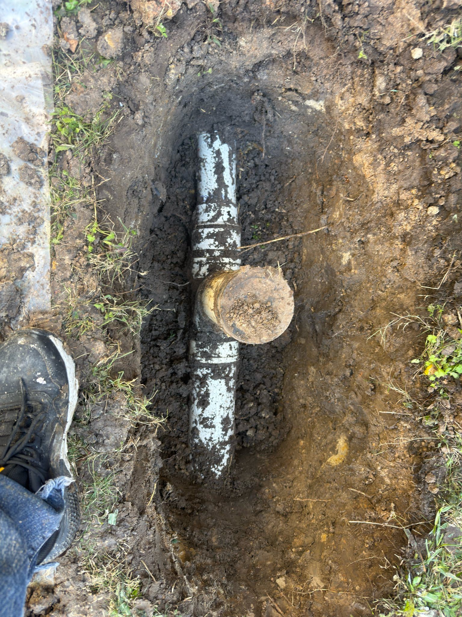 Broken pipe with capped end in muddy soil, next to a boot and grass