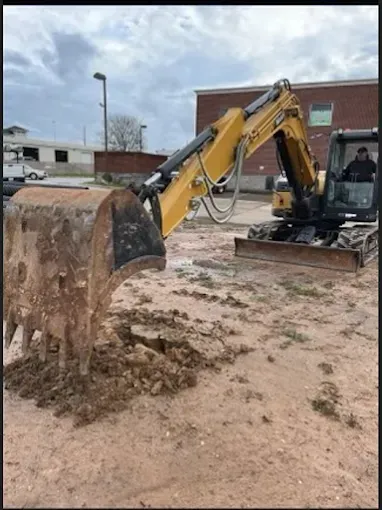 Yellow excavator with bucket digging muddy ground near a brick building