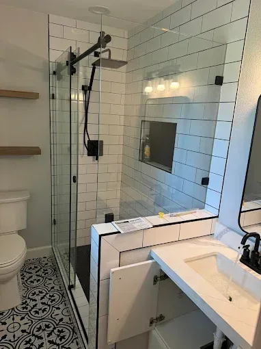 Modern shower and sink in a small bathroom with white tile and black-and-white floor pattern