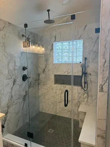 Modern glass shower with marble-look tile, black fixtures, and frosted window with built-in shelf.