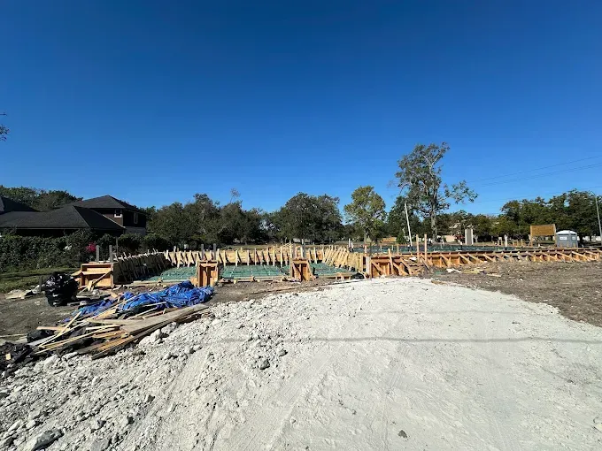 Construction site with concrete slab, wooden framing, and blue tarp under a clear blue sky