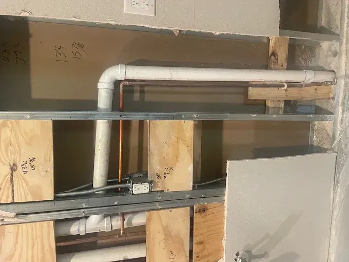 Exposed HVAC ducting and metal framing inside a wall under construction, with plywood supports.