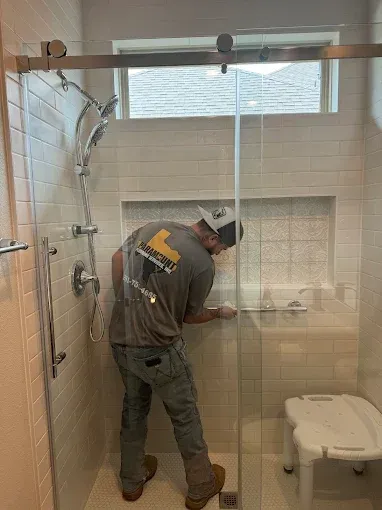Worker installing tile in a shower with a glass door and built-in niche.