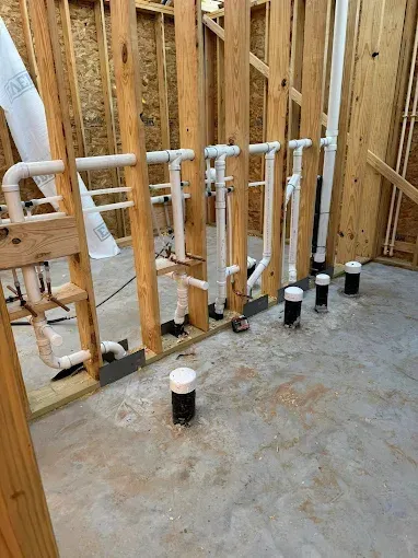 PVC plumbing pipes installed in an unfinished wooden-framed room with concrete floor holes
