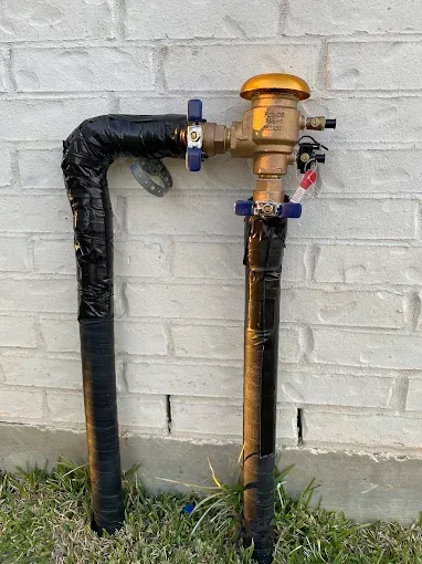 Two rusted pipes with valves against a white brick wall, one capped with an orange cover.