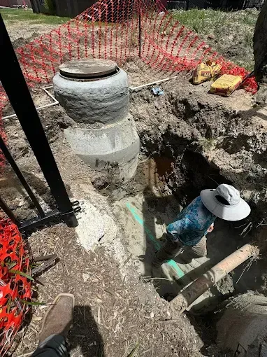 Construction workers in a trench beside a concrete structure, with orange safety fencing nearby.