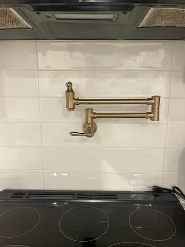 Kitchen stove beneath brass pot-filler faucet and white tiled backsplash