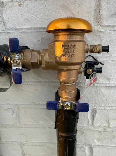 Brass plumbing valve with blue handles and black pipe mounted on a white brick wall