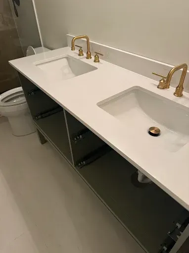 Modern bathroom vanity with two white sinks and gold faucets, cabinet doors open below