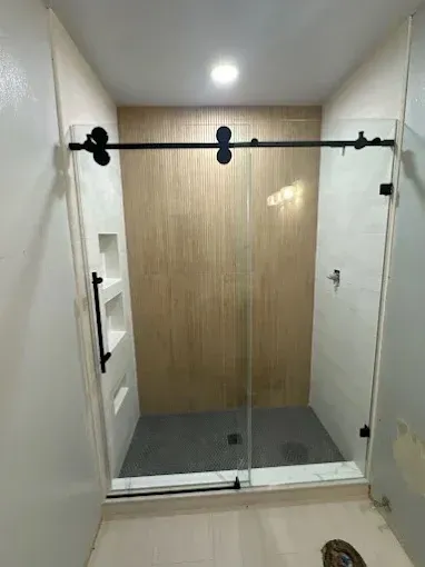 Glass shower stall with gray floor, white walls, and wood-paneled back wall