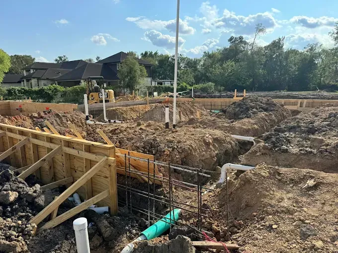 Construction site with excavated ground, wooden framing, and PVC pipes under a clear sky.