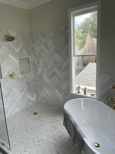 Partially tiled bathroom with a white freestanding tub, herringbone shower wall, and window view outside