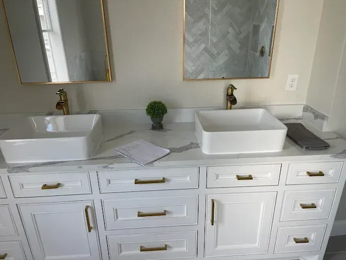 Modern bathroom vanity with two vessel sinks, gold faucets, and marble countertop under mirrors