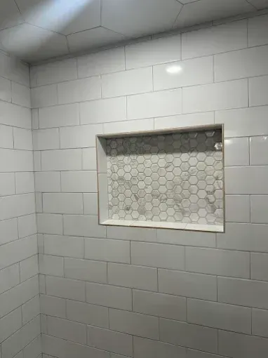 White tiled shower wall with a recessed niche and hexagon mosaic tile insert