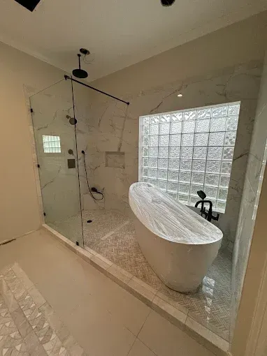 Modern bathroom with freestanding tub, glass shower, tiled walls, and large frosted window.