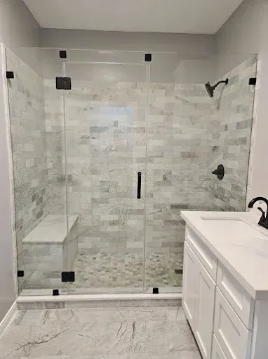 Modern bathroom with glass shower, light gray tile, and white vanity.
