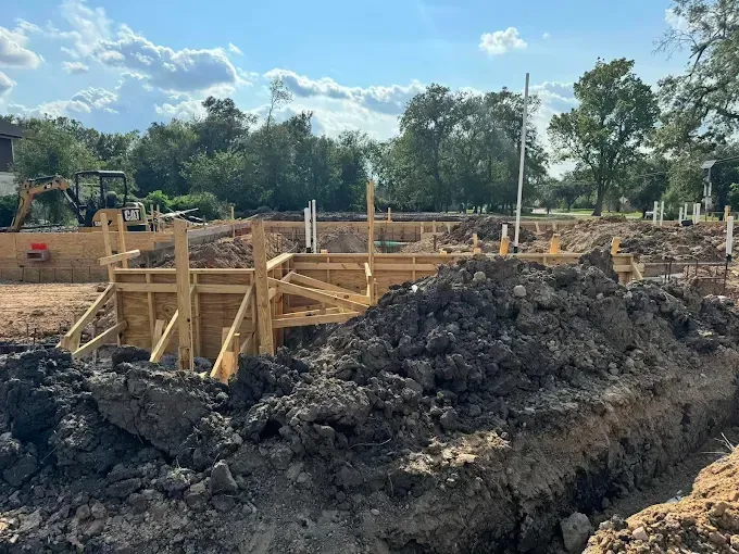 Construction site with wooden foundation forms and large piles of dark soil under a blue sky
