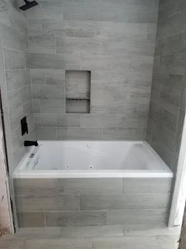 Small bathroom alcove with a white tub, gray tile walls, and a recessed shelf niche