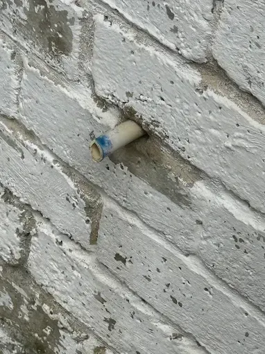 Small white pipe protruding from a white-painted brick wall with a blue cap on the end