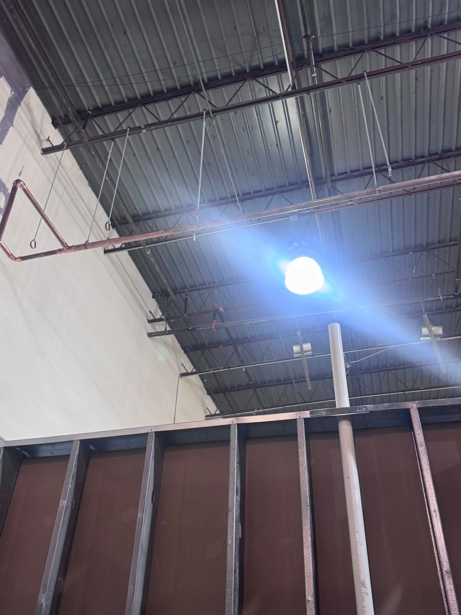 Industrial ceiling with bright overhead light and red pipework above a wall and partition.