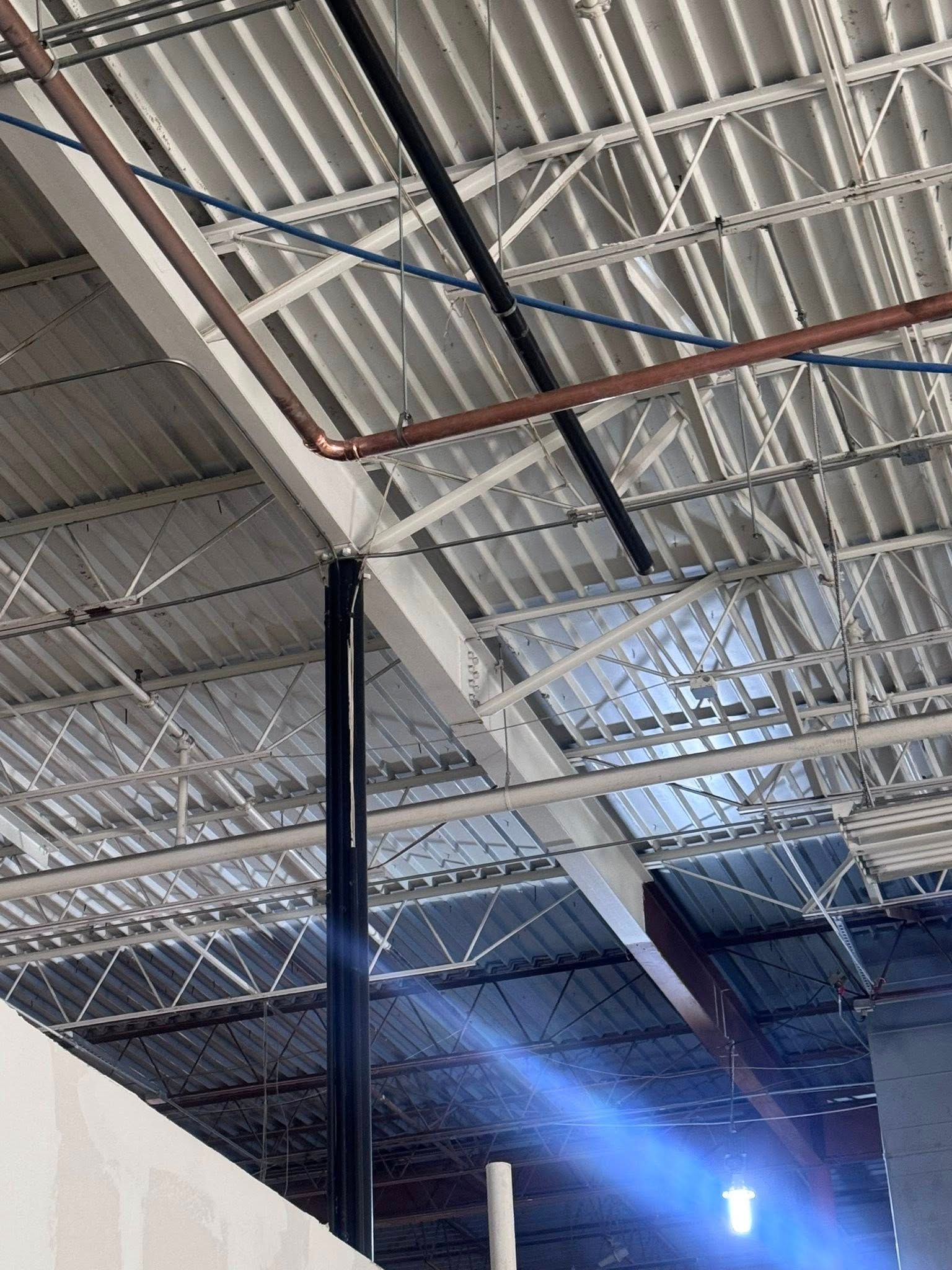 Ceiling with exposed metal beams, skylights, and a hanging light in an industrial interior